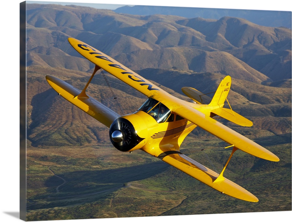 Photograph of a Beechcraft D-17 Staggerwing single propeller biplane flying over rolling hills.