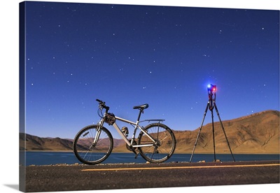 A camera, tripod and bicycle on a full moon night at Yamdrok Lake, Tibet, China