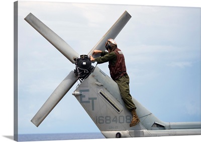 A Marine conducts maintenance on the tail of an UH-1N Huey helicopter