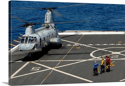 A plane captain signals to a CH-46E Sea Knight helicopter