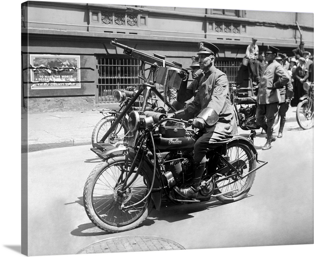 A police officer leading a parade in New York City with a machine gun mounted onto his motorcycle.