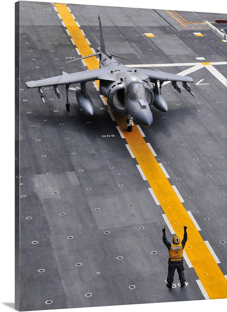 Airman directs an AV-8B Harrier II aircraft on the flight deck of USS Peleliu.