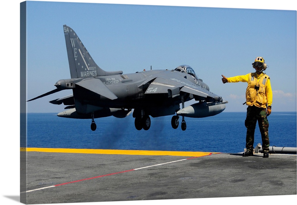 Airman gives the thumbs-up signal as an AV-8B Harrier takes off from the flight deck of USS Essex.