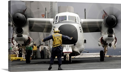 An aircraft director guides a C-2A Greyhound aircraft across the flight deck