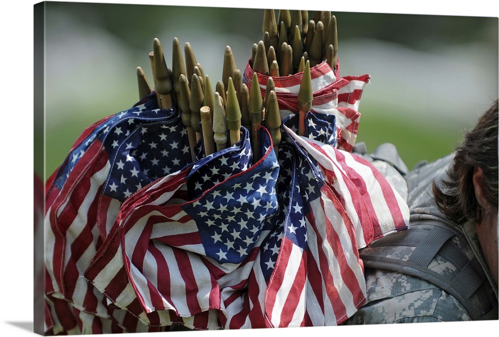 An Army soldier's backpack overflows with small American flags.