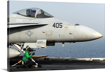 An aviation boatswain's mate guides an F/A-18C Hornet into a catapult