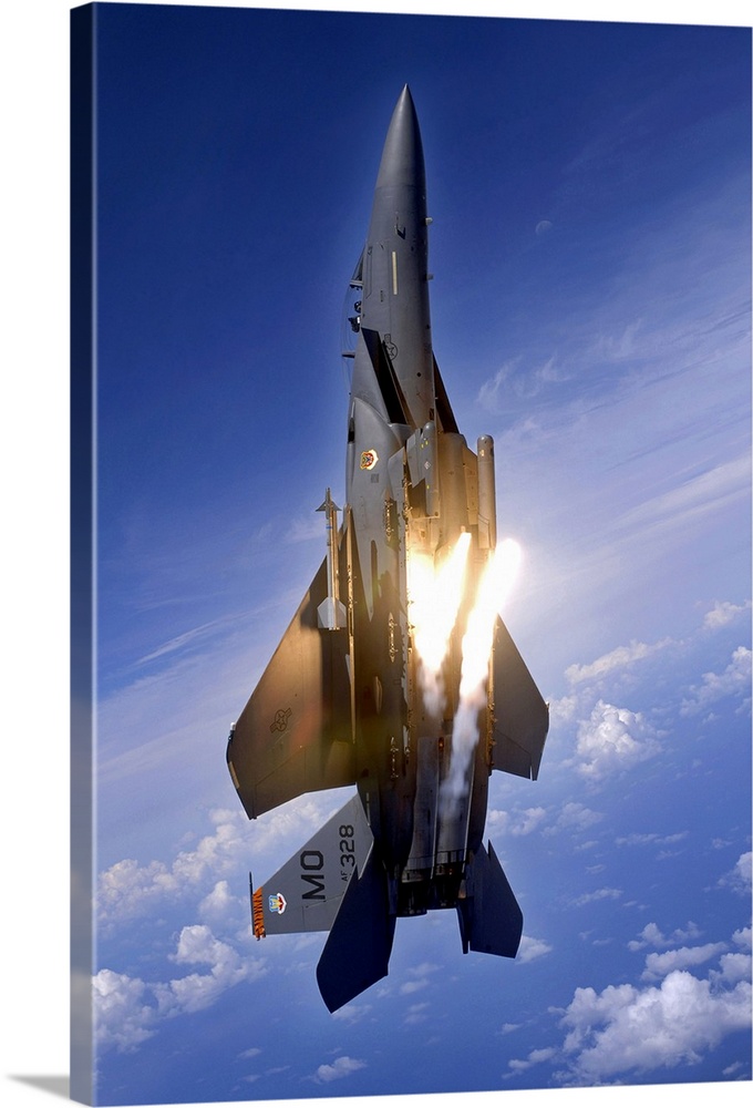Vertical panoramic of American all-weather multirole fighter launching flares as it travels upward through cloudy sky.