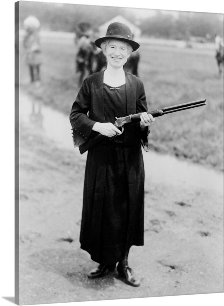 Annie Oakley standing in a black hat and dress while holding a rifle Buffalo Bill gave her, 1922.