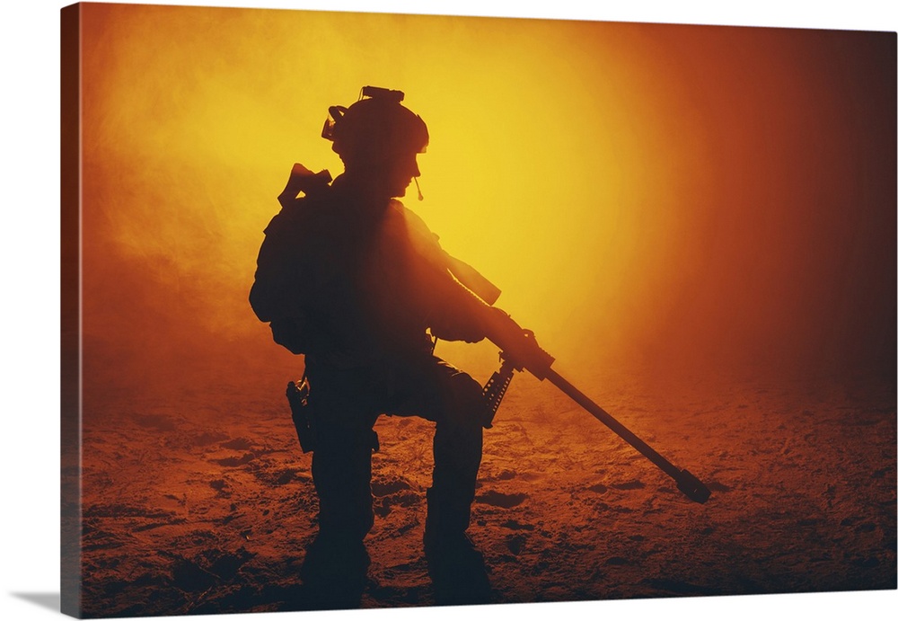 Army sniper with large caliber rifle kneeling in the fire and smoke.