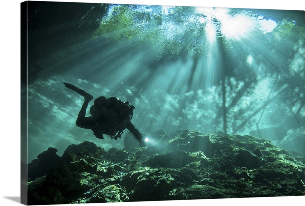 Diver passes through light beams in Chac Mool cenote in Mexico.