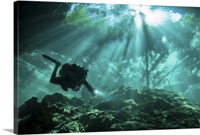 Diver passes through light beams in Chac Mool cenote in Mexico