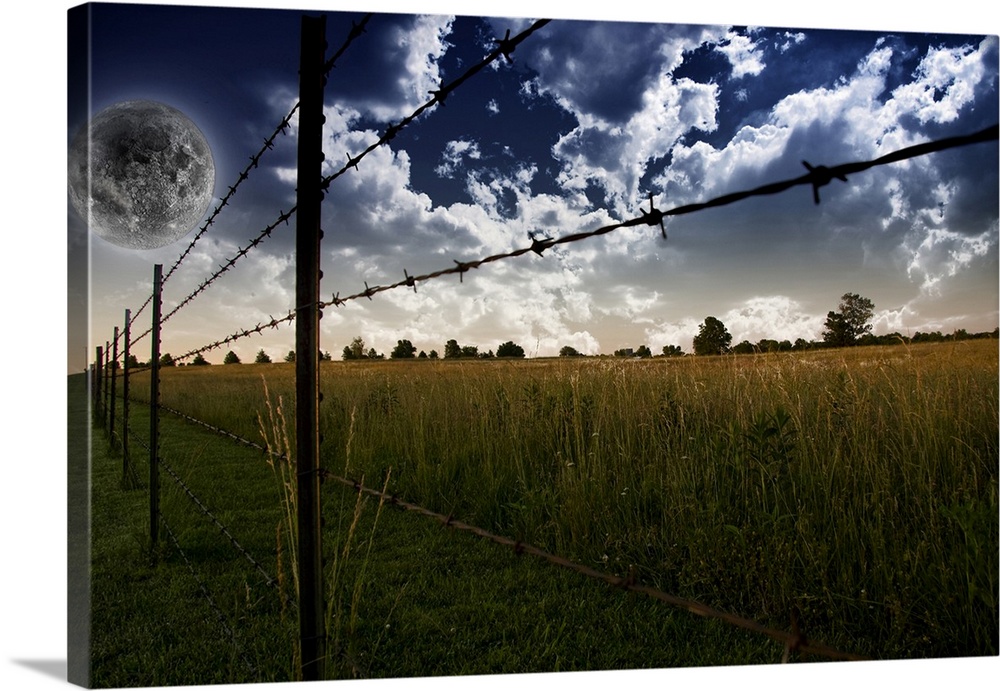Fence on a farm field with giant full moon in a cloudy sky.