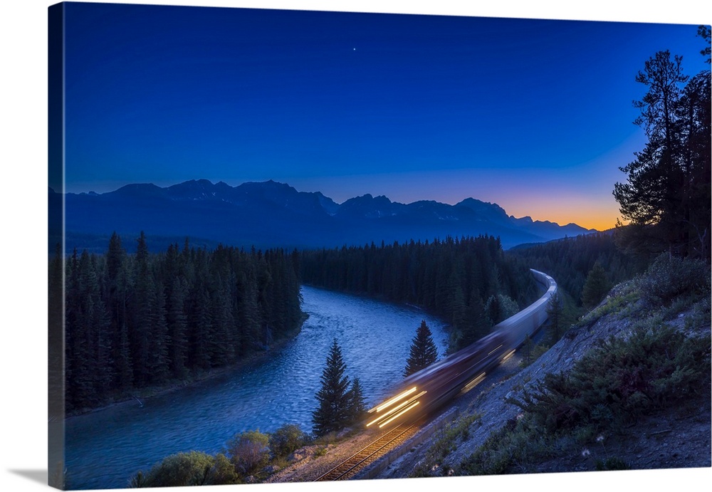 Freight train traveling through the Canadian Rockies in evening twilight with bright Venus in the sky above