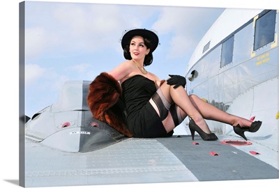 Glamorous woman in 1940's style attire sitting on a vintage aircraft