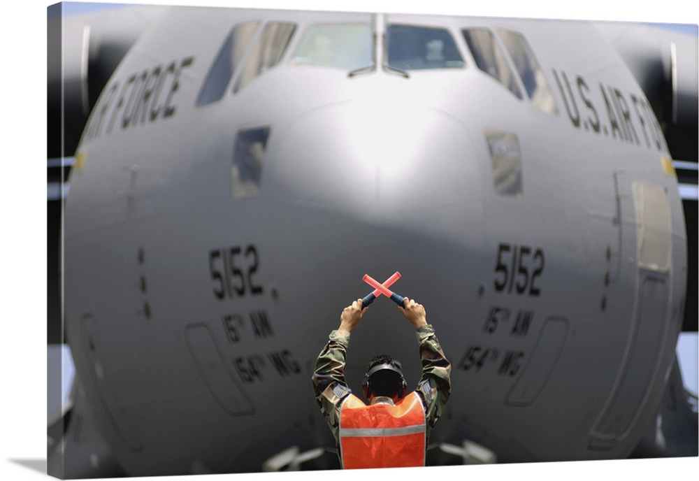Ground crewmember marshals a C-17 Globemaster III to its parking spot.