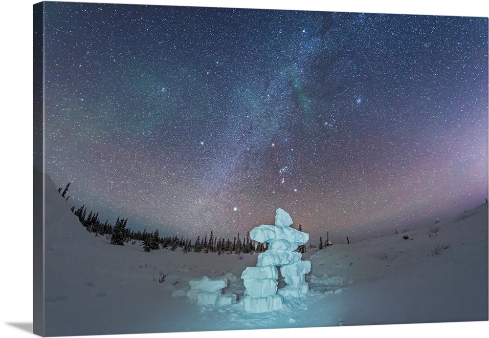 Milky Way and winter stars over a mock-up inukshuk figure made of snow, Canada.