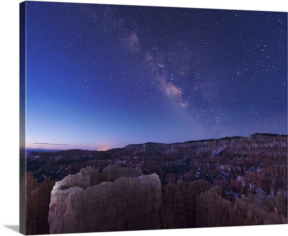 The rising sun begins fading away the nightime Milky Way over the needle rock formations of Bryce Canyon, Utah.