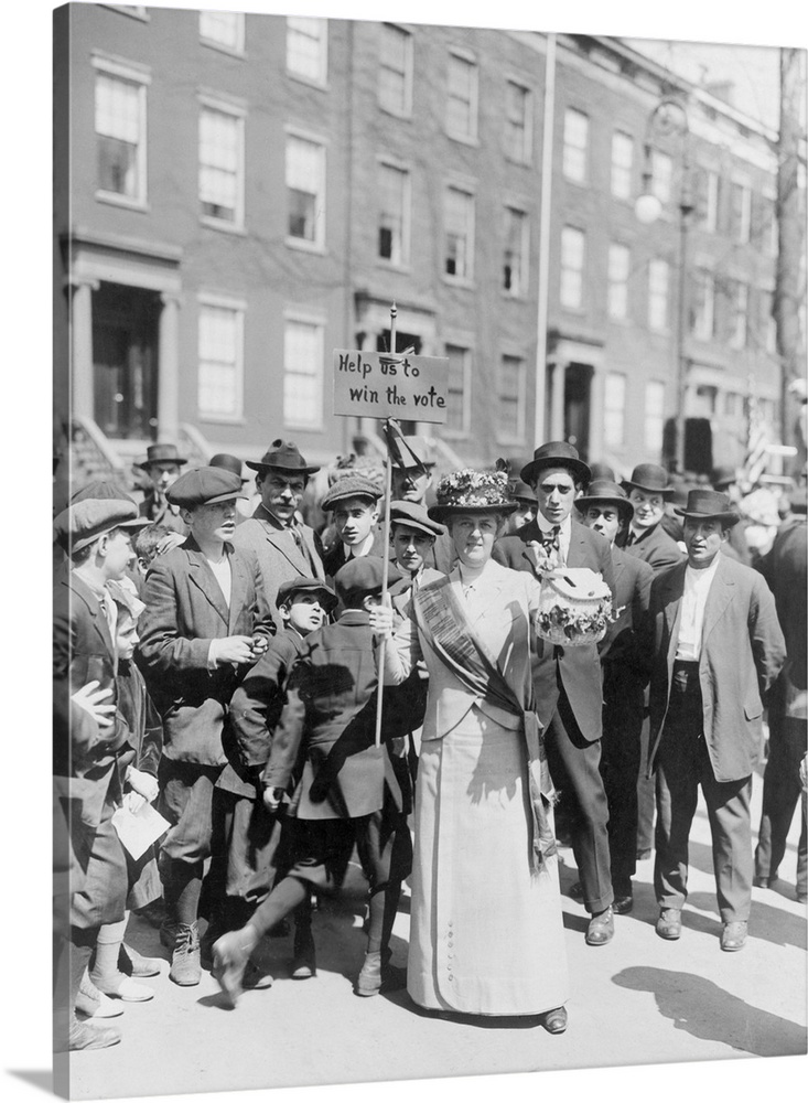 Mrs. Suffern wearing a sash and carrying a sign, surrounded by a crowd of men and boys, 1914.