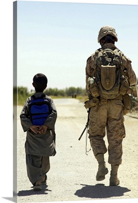Rear view of US Marine walking through Nawa bazaar with an Afghan boy in Afghanistan