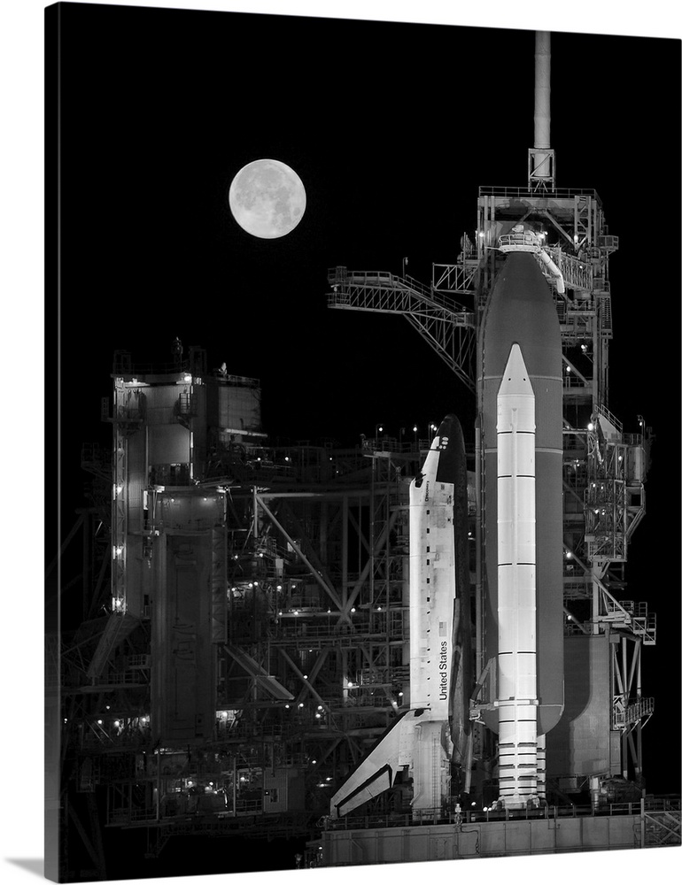 Space Shuttle Discovery sits atop the launch pad with a full moon in background.