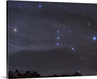 The Orion constellation rises over a hill through high thin clouds