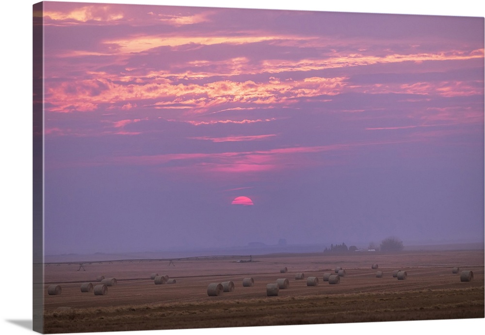 The Sun setting in a smoky and cloudy sky over a harvested grain field in southern Alberta, Canada