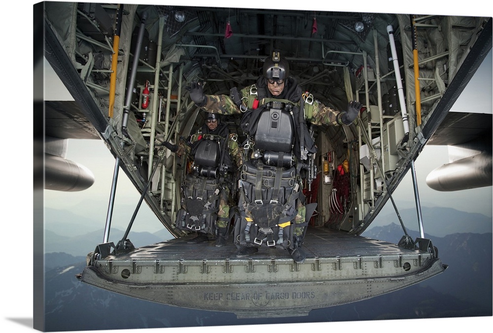 Landscape photograph of a U.S. Navy SEAL combat diver, loaded with gear, preparing to jump from the back of a C-130 Hercul...