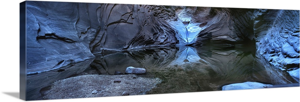Photograph of a cave illuminated in blue with still water reflecting all the rocks around.