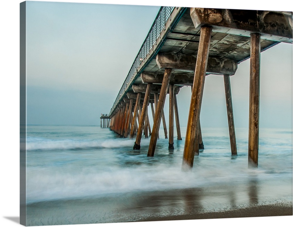 View from below a wooden pier stretching out into the ocean.