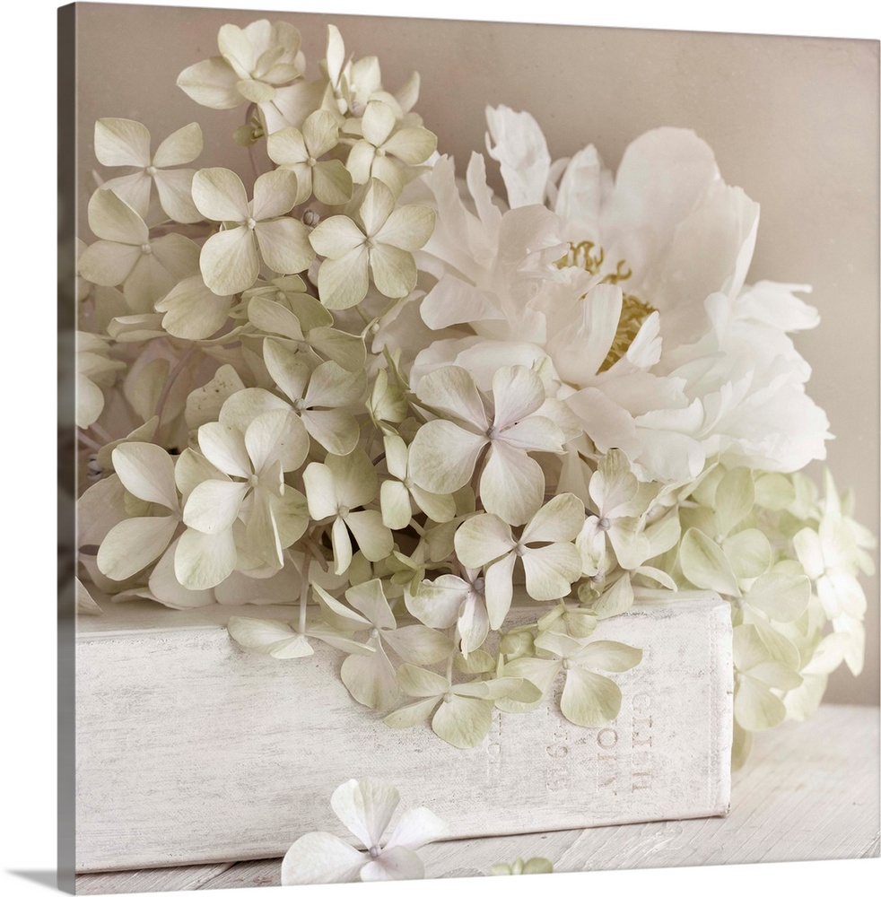 Square photo on canvas of white flowers laying on top of a white book with the spine facing the camera.