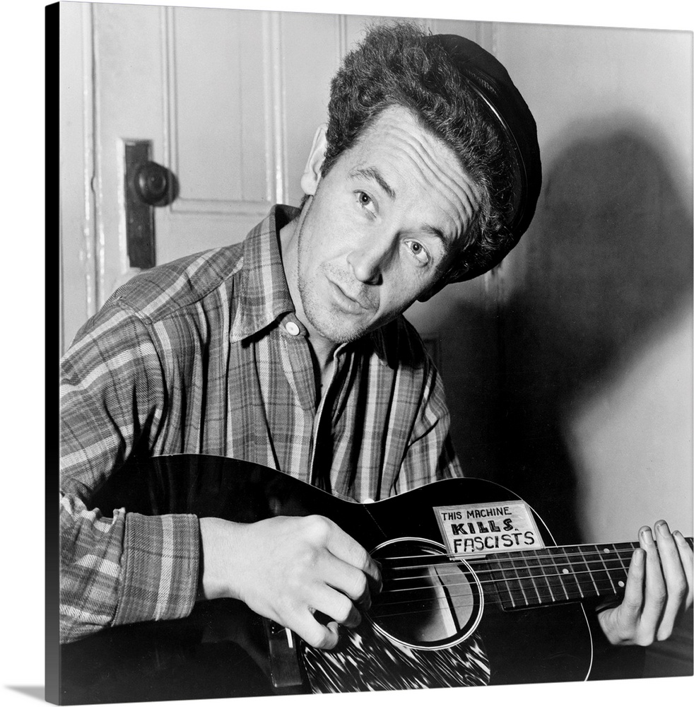 American folk singer. Photographed playing a guitar that has a sticker attached reading: 'This Machine Kills Fascists.' Ph...