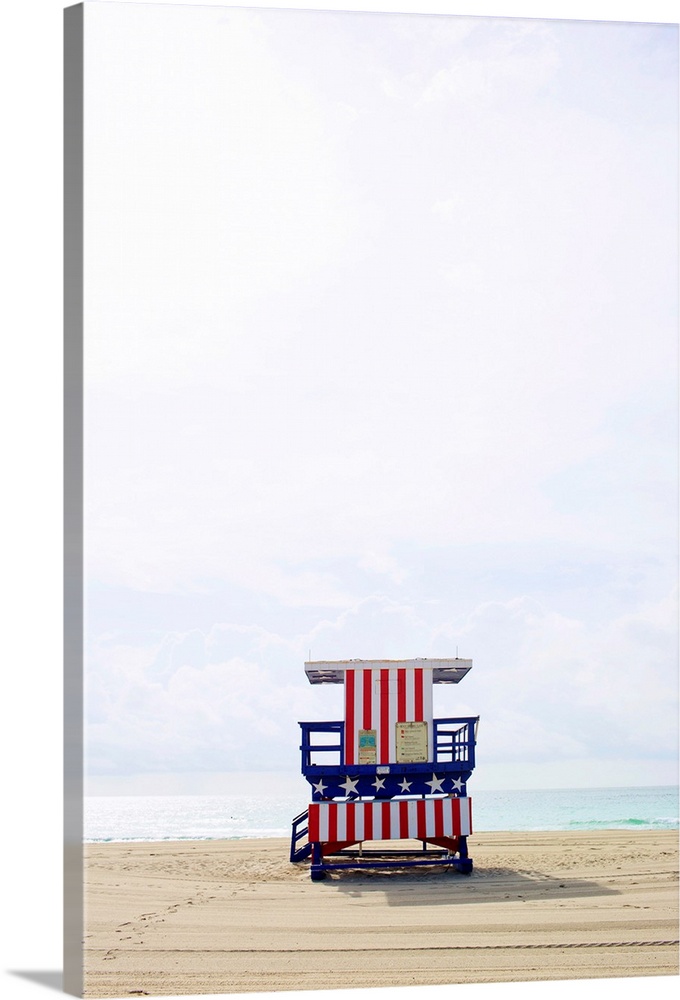 Vertical photograph of an America themed lifeguard stand on an empty beach with calm waters and a cloud filled sky.