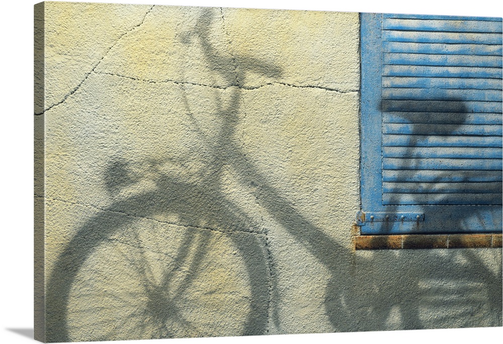 Photograph of the shadow of a bicycle on a wall and blue shutters.