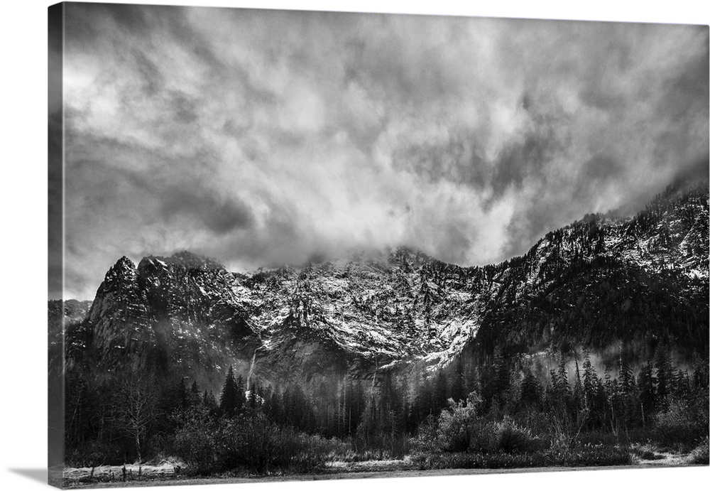 A black and white photograph of snow cover mountains and a heavy clouded sky.