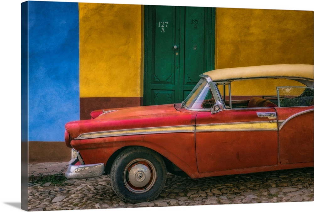 A bright red vintage car parked against a yellow and blue wall with a green door in the streets of Havana, Cuba.