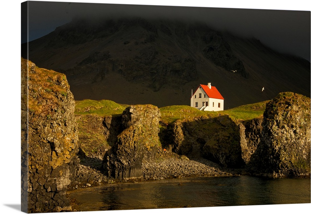 A small white house with a red roof on the steep cliffside of Snaeflesnes, Iceland.