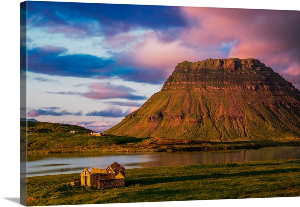 A small house near a mountain with pink clouds at sunset in Iceland.