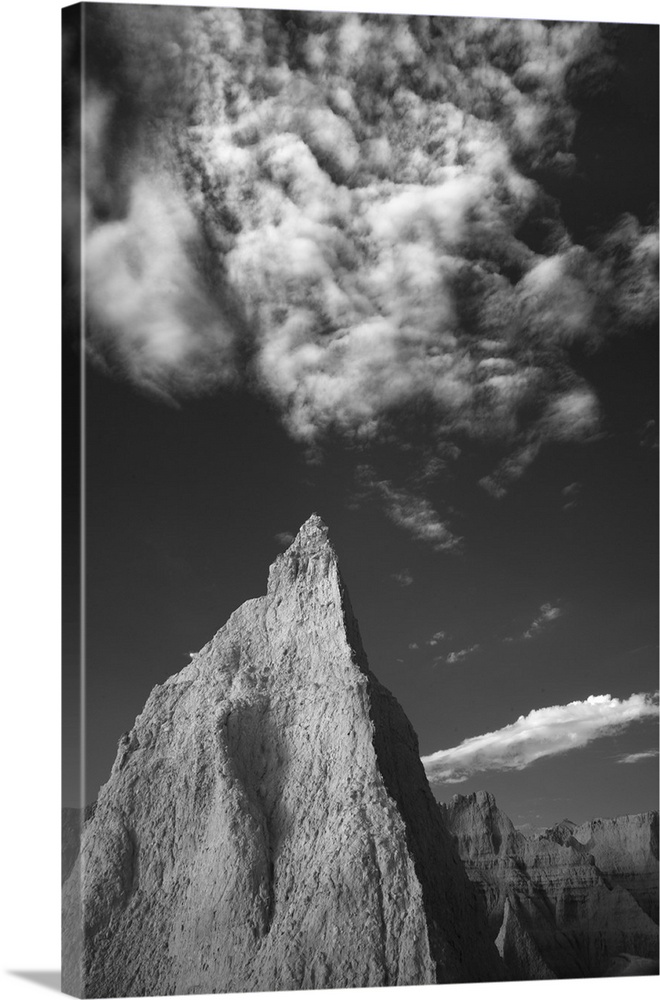 Black and white photo of a tall rock formation pointing towards clouds in the sky in the Badlands, South Dakota.