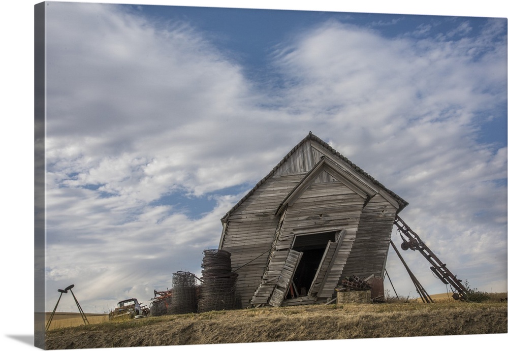 Abandoned schoolhouse building leaning heavily to the side, against a backdrop of clouds, Palouse, Washington.