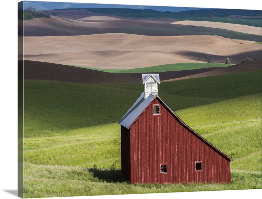 Lone red barn in a green field in the hills of the Idaho countryside.