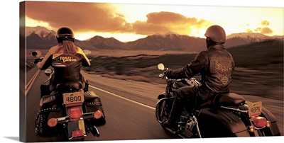 A couple ride their motorcyles alongside of each other while cruising at sunset
