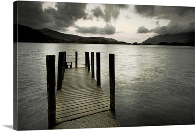 A small wooden jetty looking out over a lake with stormy clouds over a dark headland