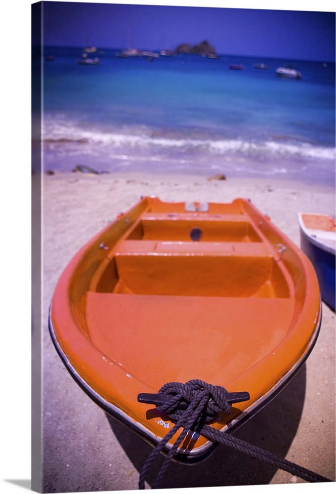 An colorful orange row boat on a Caribbean beach in front of the turqoise Caribbean Sea.