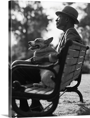 An elderly man sits on a park bench with his dog on his lap