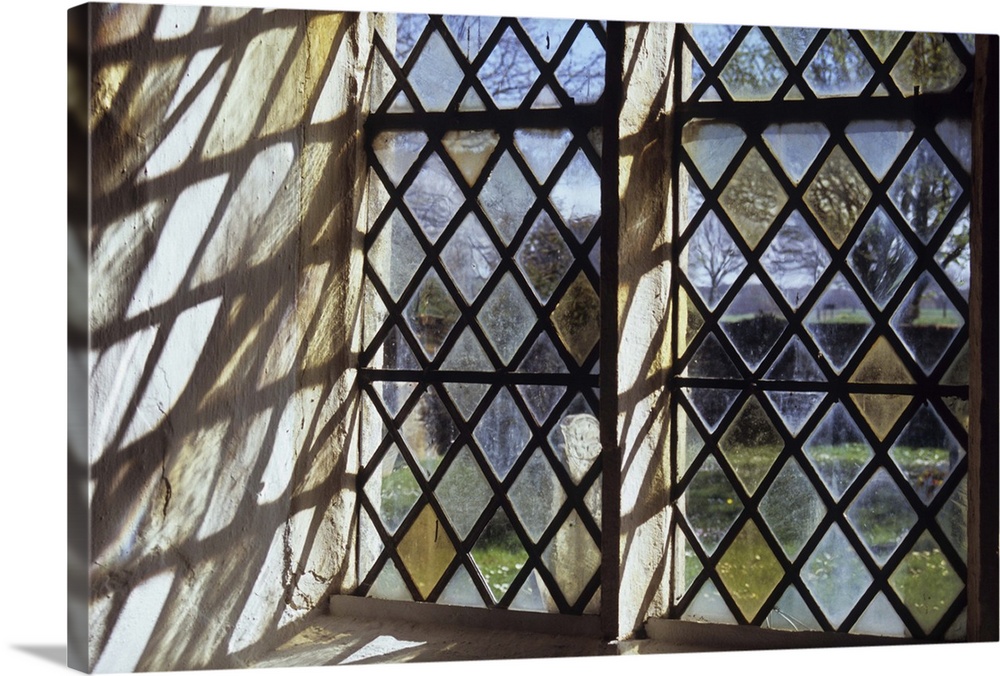 Detail of stone-framed church window with diamond-leaded panes of clear or pale yellow glass throwing interesting shadows