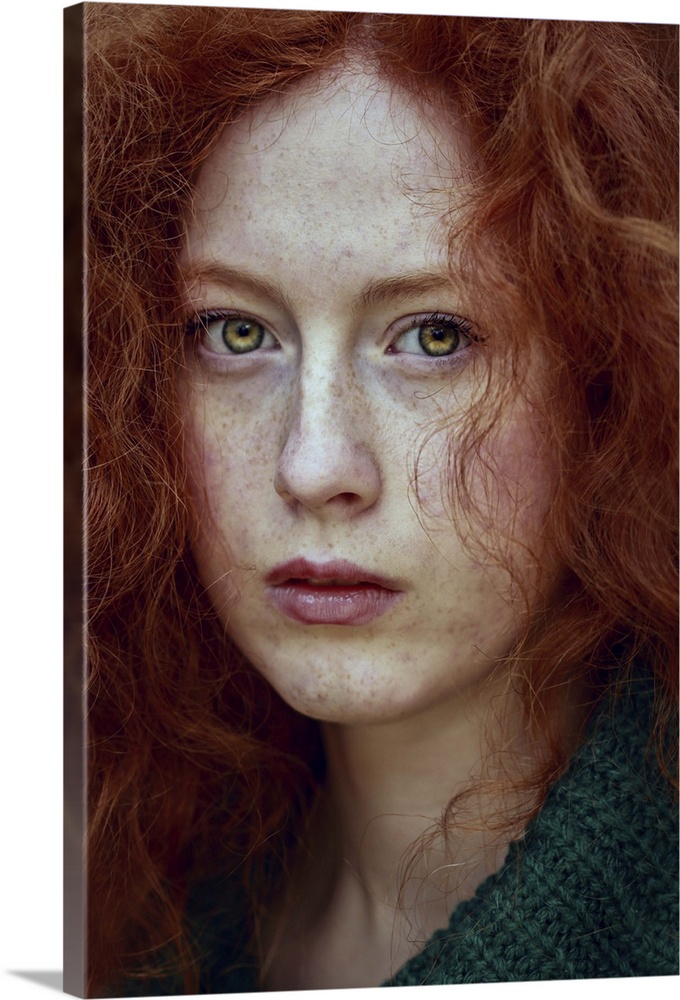 Close-up portrait of female youth with red curly hair and piercing green eyes.