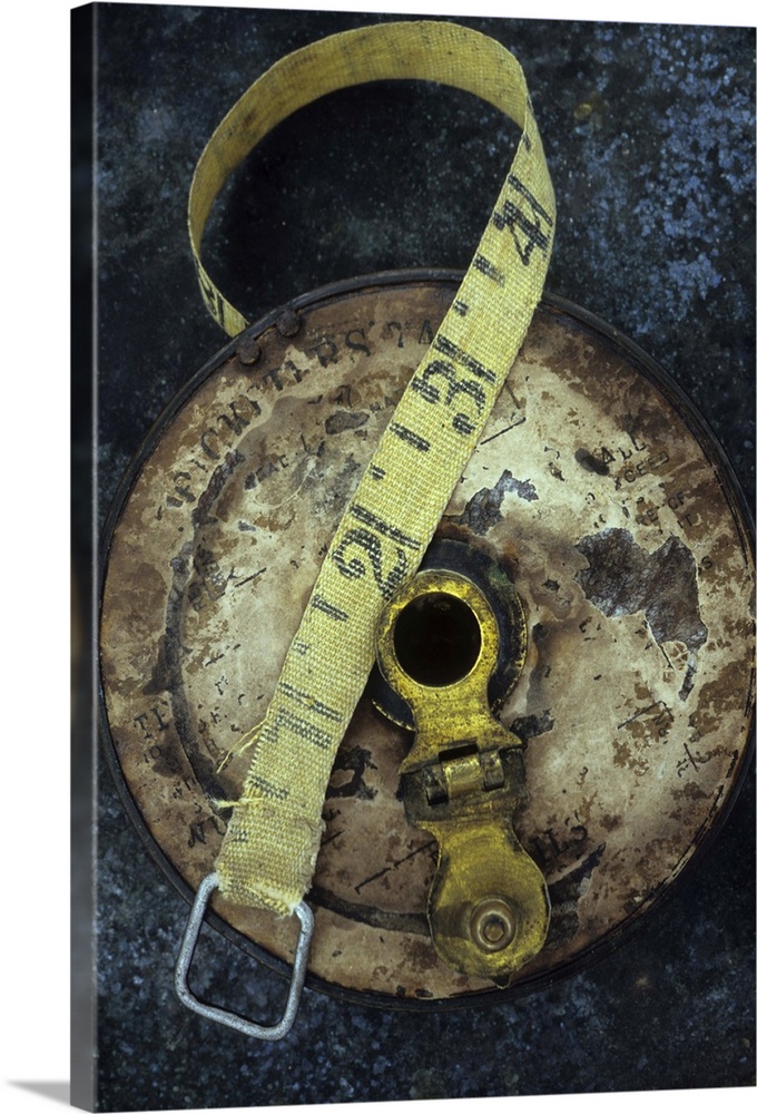 Groundsmans measuring tape in well worn metal case with brass winding handle lying on tarnished metal sheet