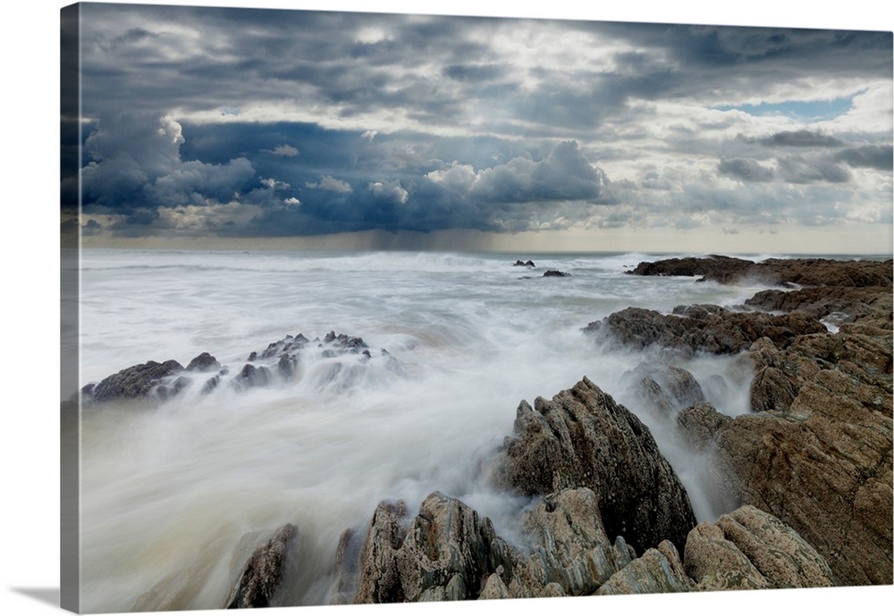 Jagged rocks on coastline with white surf under grey storm clouds