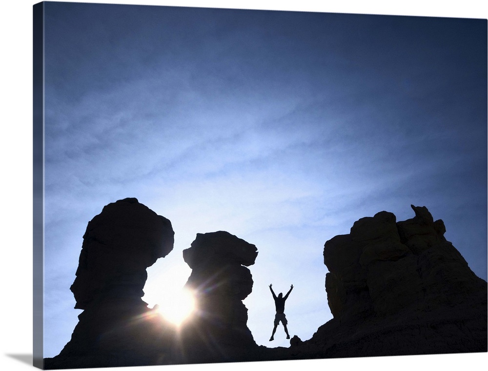 man with arms raised and jumping with sunshine surrounded by silhouetted sandstone rock formation pinnacles.  mesa de cuba...