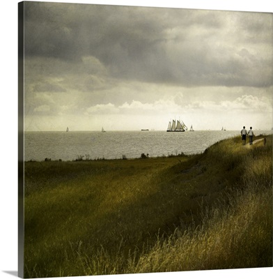 Man and woman walking along a path by the sea with tall ships